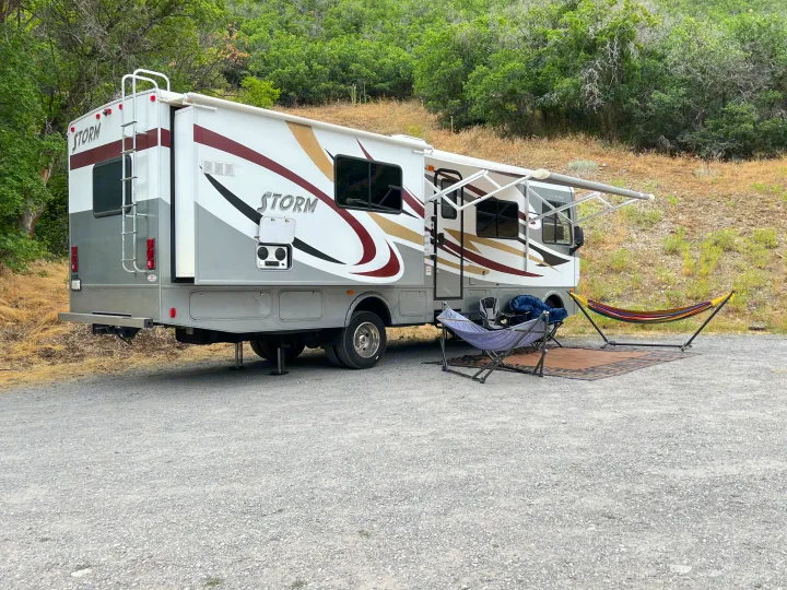 This RV rental (Fleetwood Storm) is set up for camping with an extended awning, two hammocks, and chairs on gravel.. Fleetwood Storm 32BH 2013