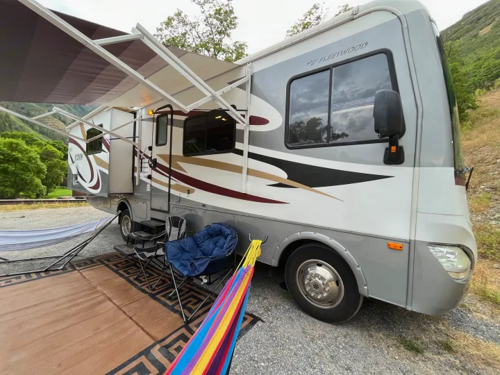 This RV rental, a Fleetwood Storm motorhome, is set up for outdoor relaxation with an awning, chairs, and hammocks at a scenic campsite.. Fleetwood Storm 32BH 2013