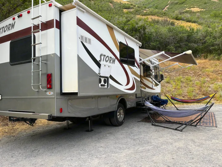 This modern RV rental motorhome offers an inviting outdoor setup with extended awnings, hammocks, and chairs for relaxing camping.. Fleetwood Storm 32BH 2013