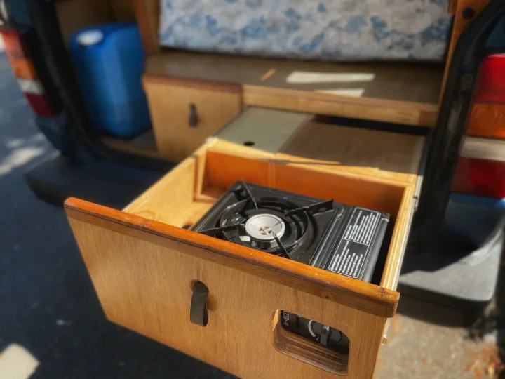 Inside an RV rental: a convenient pull-out drawer reveals a portable butane stove. Ideal for camping.. Toyota Hiace 1985