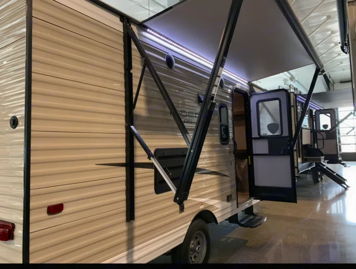 RV rental: Beige travel trailer with extended awning and open door in a showroom, hinting at adventure.. Keystone RV Hideout 2019