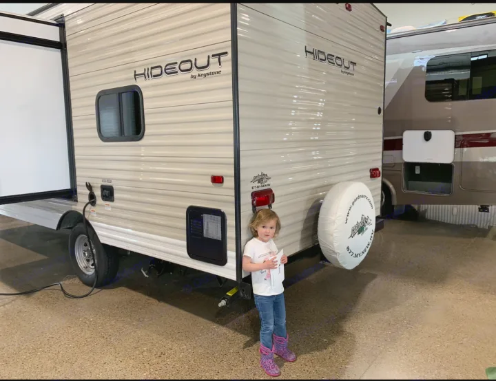 This Hideout travel trailer by Gardner RV, a great option for an RV rental, is seen in a showroom with a child nearby.. Keystone RV Hideout 2019