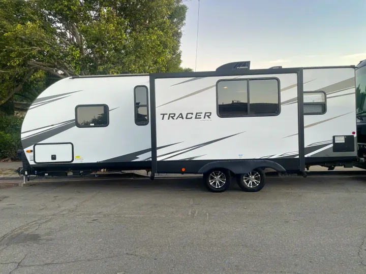 This white Tracer travel trailer RV rental, with a slide-out and modern graphics, is parked on asphalt.. Prime Time Tracer 2021