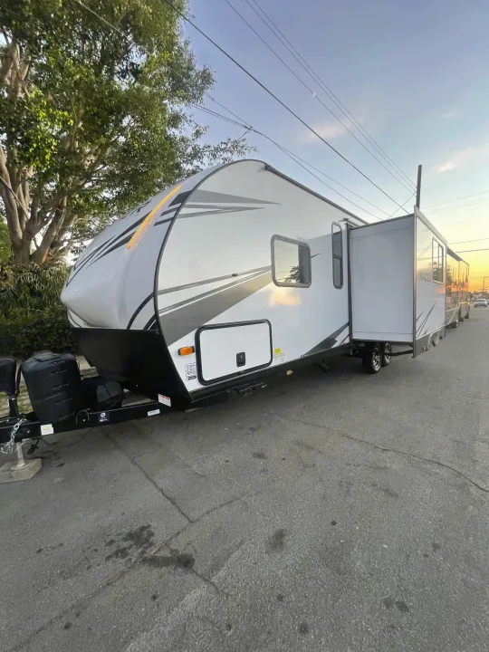 A large white and grey travel trailer RV rental, with an extended slide-out, is parked on asphalt.. Prime Time Tracer 2021