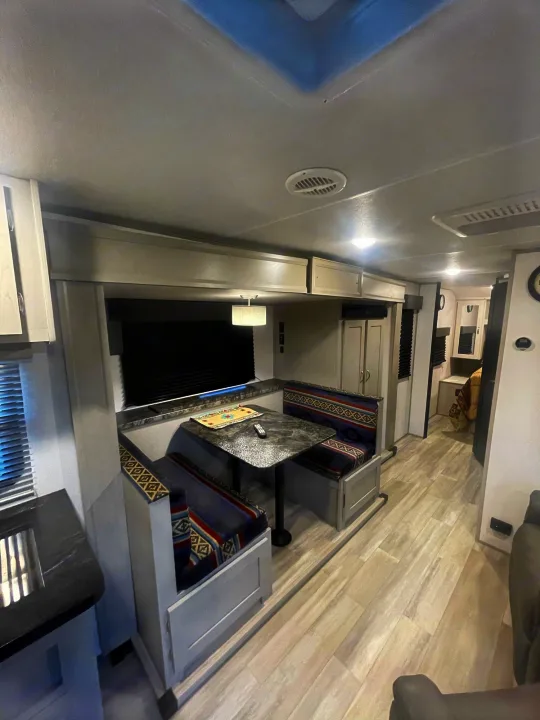 Bright RV rental interior with a dining booth, kitchen, and light flooring leading to the rear living space.. Prime Time Tracer 2021