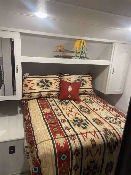 Cozy RV rental bedroom features Southwestern bedding, overhead storage, and decorative desert art.. Prime Time Tracer 2021