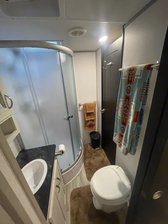 Inside an RV rental bathroom: compact curved shower, vanity, toilet, and patterned towels. Practical for travel.. Prime Time Tracer 2021