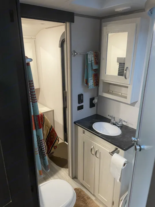 RV rental bathroom featuring a sink, vanity, toilet, and an open doorway to the bedroom. Clean, functional layout.. Prime Time Tracer 2021