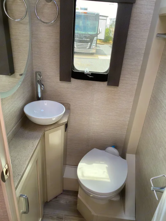 A well-appointed RV rental bathroom with a white vessel sink, sleek chrome faucet, toilet, and window offering an exterior view.. Tiffin Motorhomes Wayfarer LW 2023