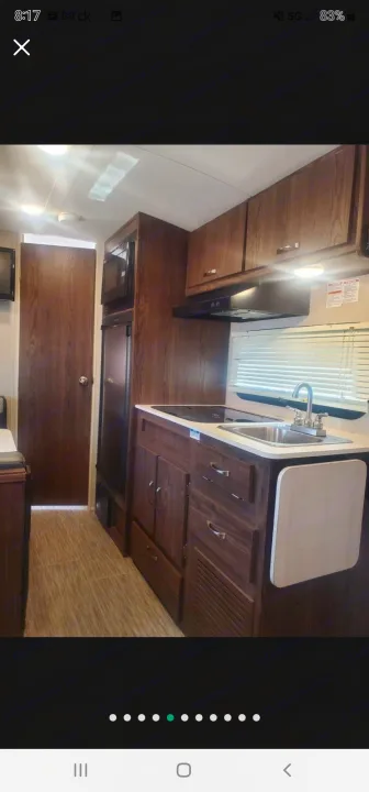 RV rental interior: Compact kitchen with dark wood cabinets, sink, stovetop, microwave, and fridge. Ideal for travel.. Forest River Rockwood Geo Pro 2018