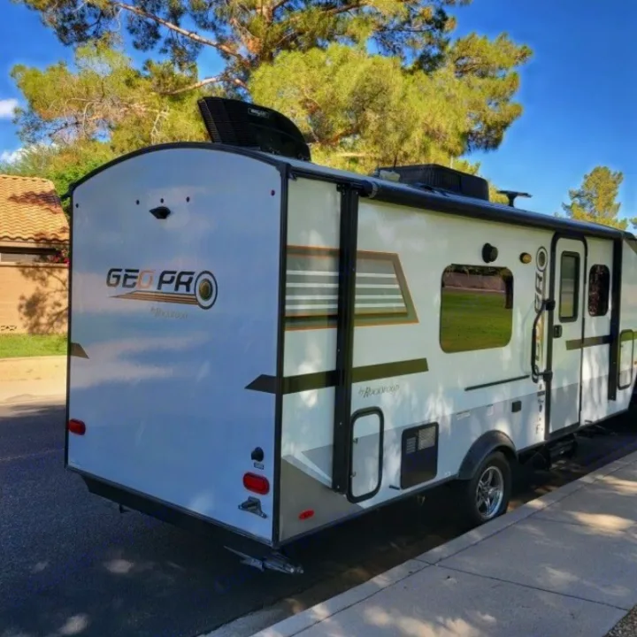 A modern white Geo Pro travel trailer (RV rental) is parked on a street, featuring a roof fan, awning, and rear lights.. Forest River Rockwood Geo Pro 2018