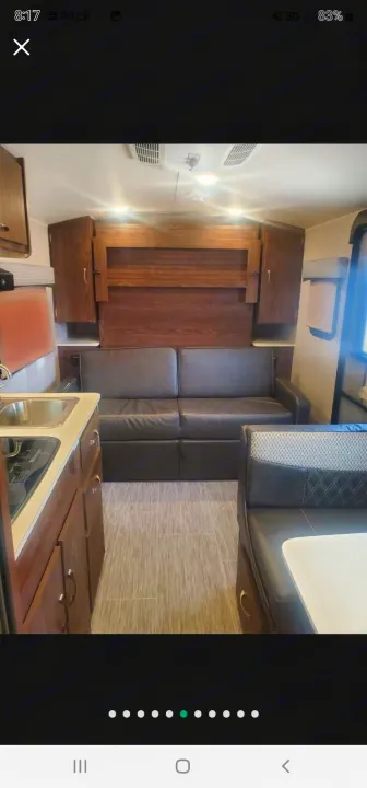RV rental interior: A modern kitchenette, black leather sofa, wood cabinets, and a dinette with patterned seats on gray flooring.. Forest River Rockwood Geo Pro 2018