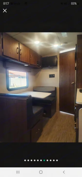 RV rental interior: dinette, wooden overhead cabinets, a wall-mounted TV, and a wooden door on the right.. Forest River Rockwood Geo Pro 2018