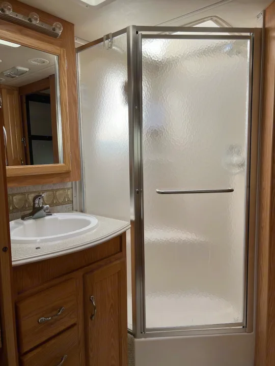 RV rental bathroom featuring a compact vanity, sink, and a frosted glass shower enclosure. Clean, functional space.. National RV Sea Breeze 2006