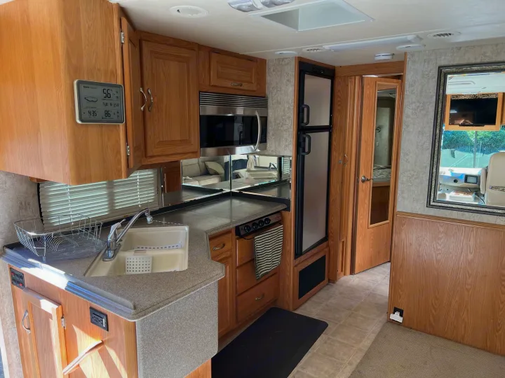 Well-equipped RV rental kitchen and living space, showing a sink, microwave, and refrigerator. Features light wood cabinetry.. National RV Sea Breeze 2006