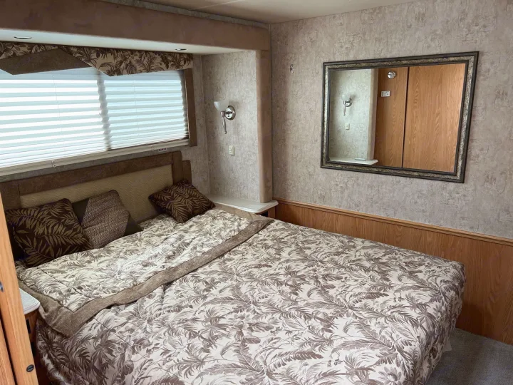RV rental bedroom view: large bed with nature-patterned bedding, window with blinds, and mirrored wall. Comfortable travel space.. National RV Sea Breeze 2006