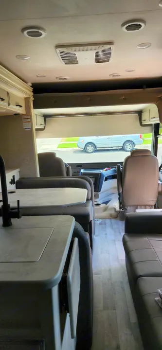Modern rv rental interior, sideways view. Shows ceiling AC, comfortable seating, kitchen counter, and window with outdoor view.. Jayco Alante 2021