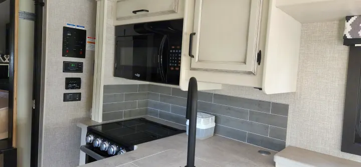 RV rental kitchen: modern cabinets, microwave, stovetop, sink, and system control panels with gray tile backsplash.. Jayco Alante 2021