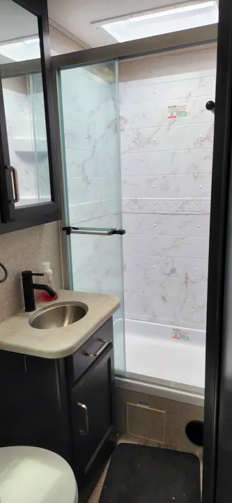 An rv rental bathroom showing a glass shower, white marble-patterned walls, a countertop sink, and a toilet. Compact travel space.. Jayco Alante 2021