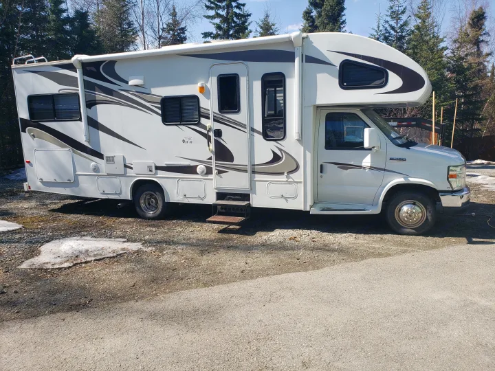 A white and gray Class C rv rental motorhome with decorative swirls, parked on a gravel lot, ready for camping adventures.. Jayco Greyhawk 2011