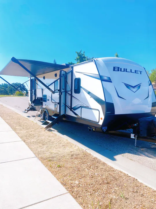 A white and black Bullet travel trailer, ideal for rv rental, is set up with an extended awning and outdoor kitchen.. Keystone RV Bullet Ultra Lite 2022