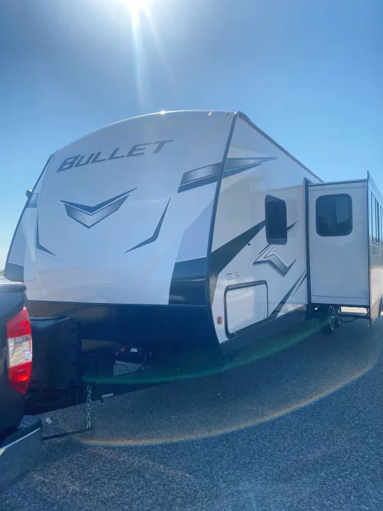 White Bullet travel trailer RV rental with extended slide-out, hitched to a pickup truck on a sunny day.. Keystone RV Bullet Ultra Lite 2022