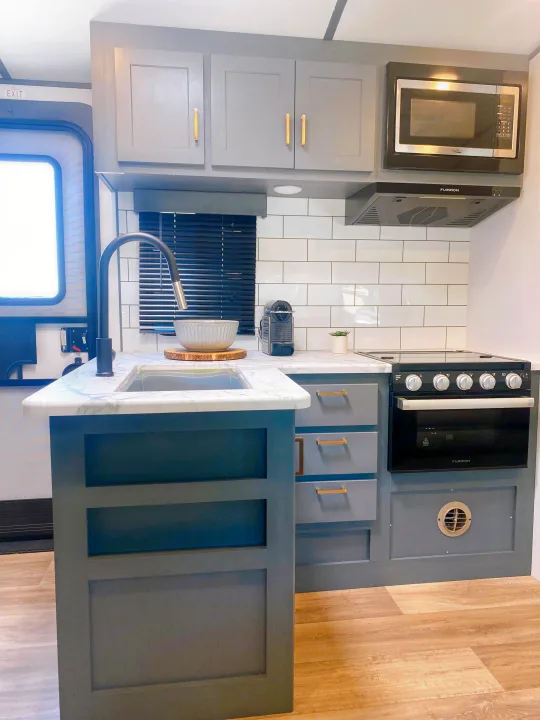 RV rental's sleek kitchen: gray cabinetry, white marble-look counters, black appliances, and subway tile backsplash.. Keystone RV Bullet Ultra Lite 2022