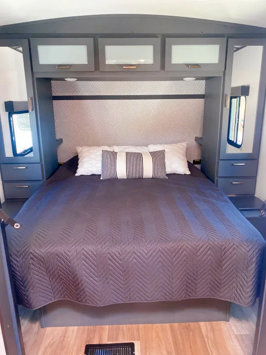 Modern RV rental bedroom with dark gray quilted bed, geometric wallpaper, and smart storage.. Keystone RV Bullet Ultra Lite 2022