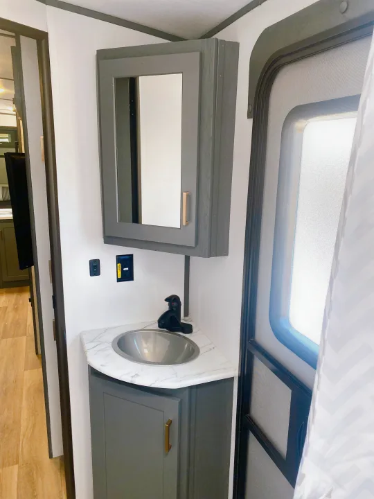 RV rental bathroom: modern gray vanity, marble-look counter, sink, mirrored cabinet, and RV screen door.. Keystone RV Bullet Ultra Lite 2022