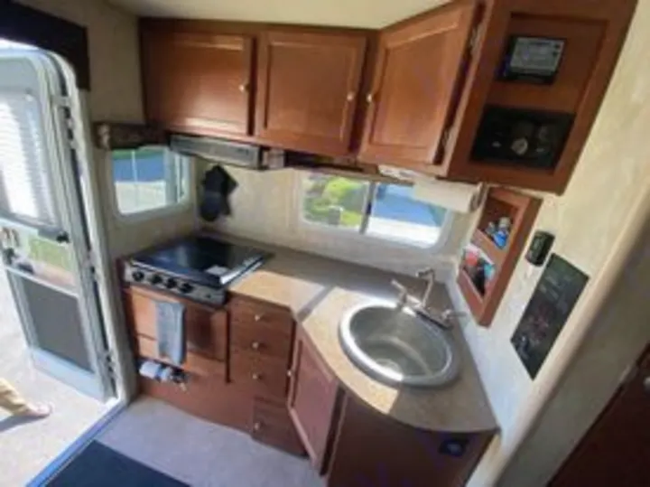 Compact RV rental kitchen interior: a practical space with a stove, sink, and ample wood cabinets for your travels.. Northwood Mfg Wolf Creek 2017
