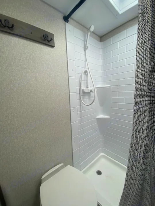 Inside an rv rental: a compact RV bathroom with a white shower stall, handheld showerhead, toilet, and wall hooks.. KZ Sportsmen LE 2021