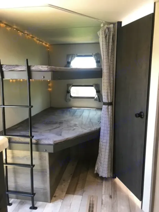 RV rental interior showing cozy bunk beds, a ladder, small windows, and string lights along the wall.. KZ Sportsmen LE 2021