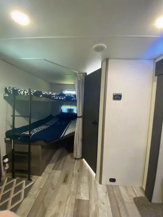 RV rental bedroom interior: a compact sleeping space with overhead storage, a wall vent, and a fire extinguisher.. KZ Sportsmen LE 2021