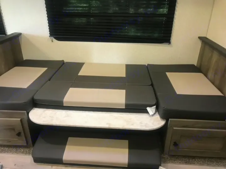 This RV rental features a dinette that converts into a bed, with grey and beige cushions, a table, and built-in storage.. KZ Sportsmen LE 2021