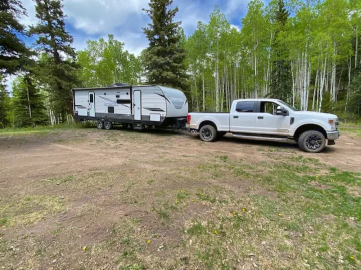 White truck towing a travel trailer RV rental at a forest campsite.. KZ Sportsmen LE 2021