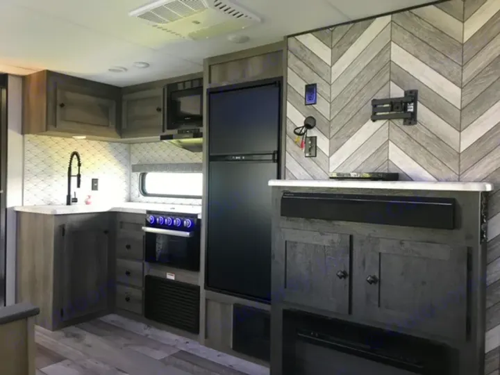 Modern RV rental interior showcasing a full kitchen with backsplash, fridge, stove, and a cozy living area with TV mount & soundbar.. KZ Sportsmen LE 2021