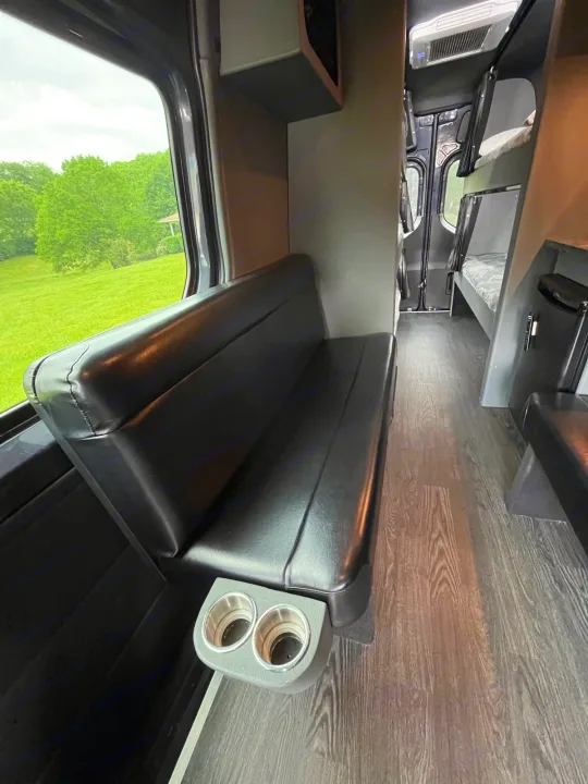 Spacious RV rental interior with comfortable seating, bunks, and scenic window views of a green landscape.. Mercedes Sprinter Motorhome Campervan RV 2021