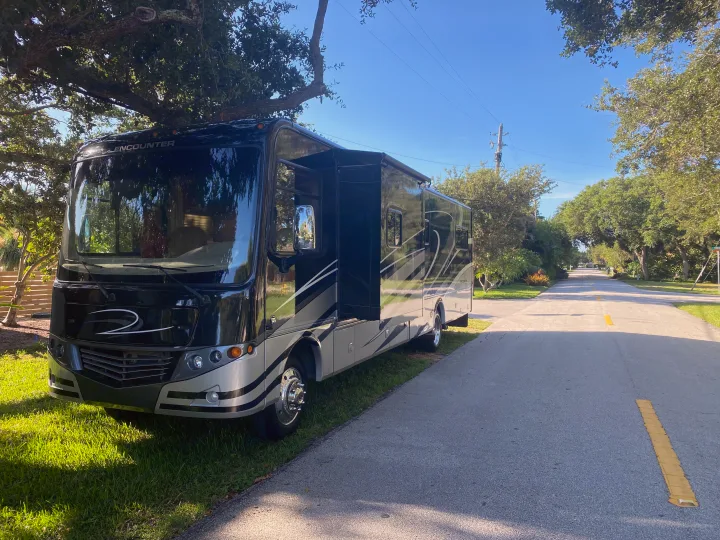 Sleek black & silver motorhome available for RV rental, parked on a sunny, tree-lined street.. Coachmen Encounter 2013