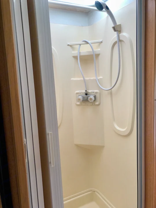 Inside an RV rental, showing a compact, cream-colored shower stall with a handheld showerhead and faucet controls.. Itasca Spirit 2001