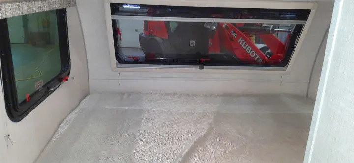 Inside an RV rental, a red Kubota excavator is seen through the window, with an "EXIT" sign visible on another window.. Forest River RPOD 190 2021