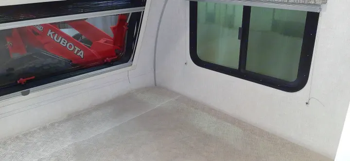 RV rental interior: two rounded windows, light textured walls/ceiling. A red Kubota is reflected, upside down, in one window.. Forest River RPOD 190 2021