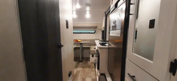RV rental interior: modern, compact kitchen with a stainless steel fridge, microwave, dinette, and hallway with a door.. Forest River RPOD 190 2021