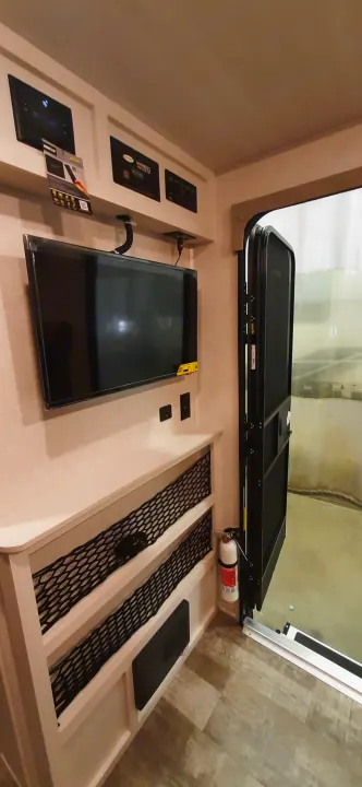 RV rental interior: A bed area with TV, control panel, fire extinguisher, and mesh storage.. Forest River RPOD 190 2021