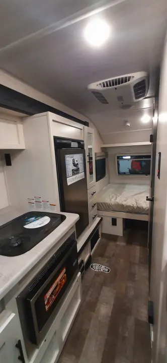 Compact RV rental interior: modern kitchen with oven, stovetop, sink, and "rPod" fridge. Bed area in back.. Forest River RPOD 190 2021