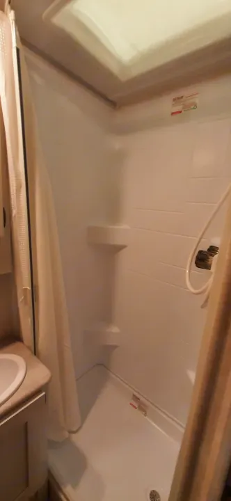 Compact RV rental shower with white walls, shower head, and drain. Functional bathroom space for your next adventure.. Forest River RPOD 190 2021