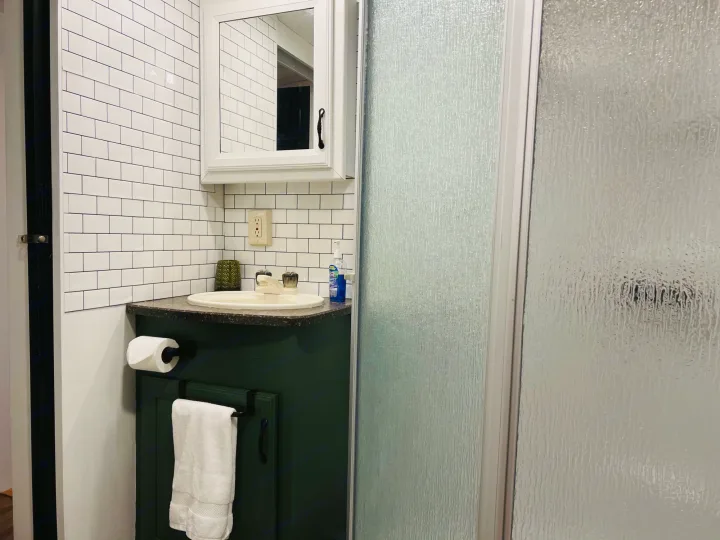 RV rental bathroom with a dark green vanity, white subway tile, sink, and a frosted glass shower stall.. Heartland RVs Greystone 2012