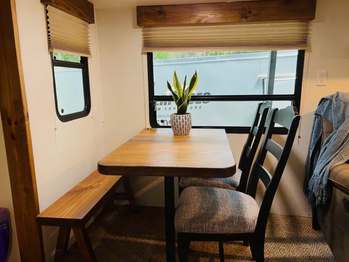 Cozy RV rental dining area: Wooden table, bench, and two upholstered chairs by windows. A plant adds a touch of green.. Heartland RVs Greystone 2012