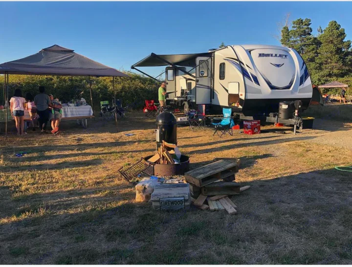 Family enjoying a spacious RV rental setup at a sunny campsite with a picnic and fire pit.. Keystone RV Bullet Ultra Lite 2020