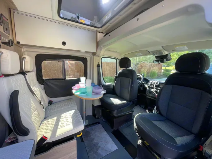 Bright RV rental interior: a cozy dining area with colorful dishes, comfortable seating, and large windows.. Winnebago Solis 2022
