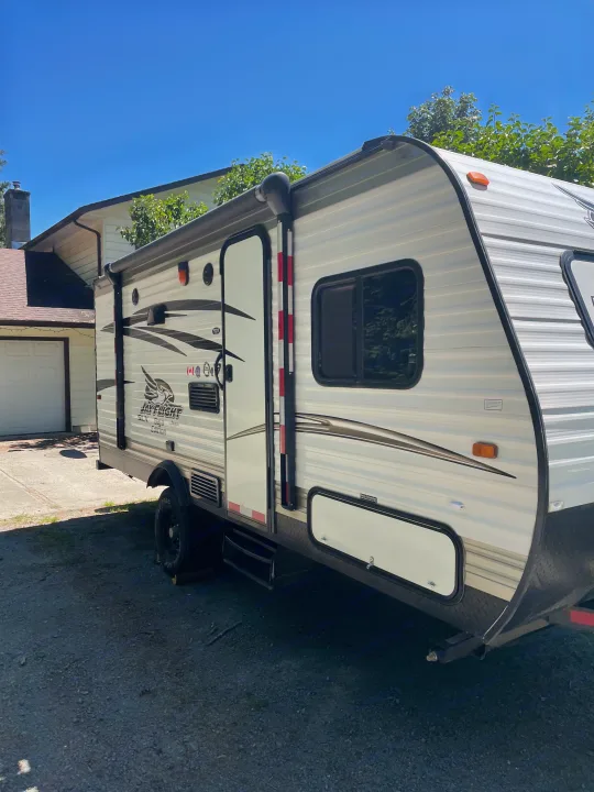 A white Jay Flight travel trailer is parked on gravel in a sunny residential setting, ready as an RV rental option.. Jayco Jay Flight SLX 2016